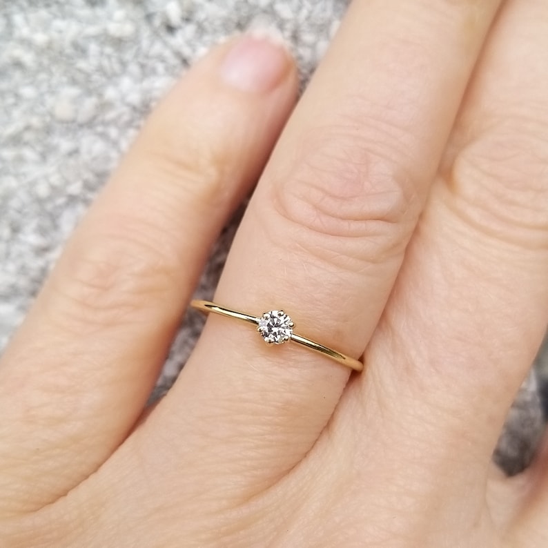 Op de afbeelding: Een delicate gouden ring met een kleine, heldere ronde edelsteen in het midden.