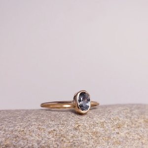 Könnte beinhalten: Ein goldener Ring mit einer Zargenfassung, in der ein ovaler, dunkelblauer Edelstein sitzt.