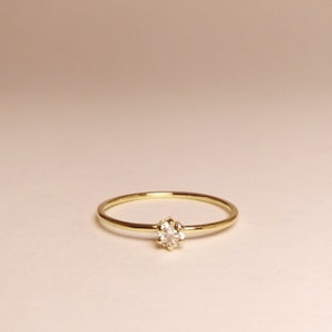 Op de afbeelding: Een delicate gouden ring met een enkele, kleine, heldere edelsteen in een kraalbezetting.