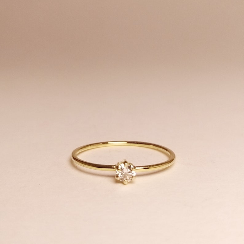 Op de afbeelding: Een delicate gouden ring met een enkele, kleine, heldere edelsteen in een kraalbezetting.