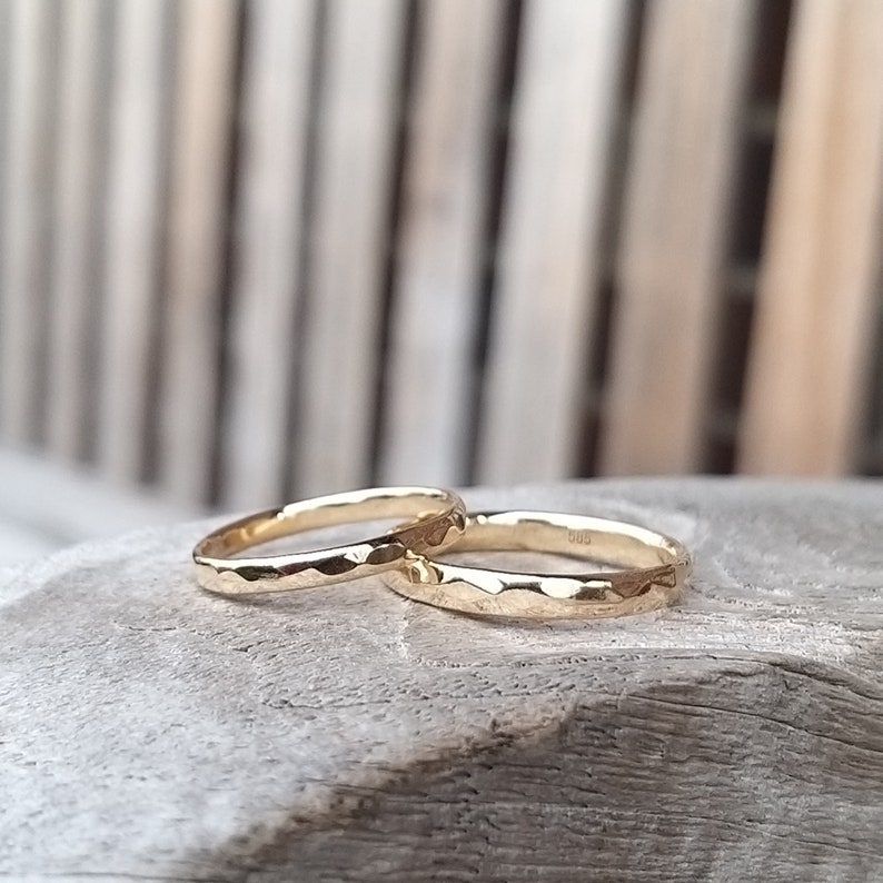 Puede incluir: Dos alianzas de oro martilladas, una ligeramente m&aacute;s grande que la otra, est&aacute;n apiladas una encima de la otra sobre una superficie de madera.