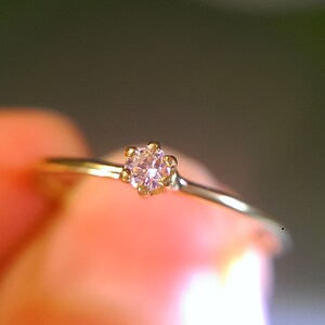 Op de afbeelding: Een delicate gouden ring met een enkele, kleine, heldere roze edelsteen in een kraalbezetting.
