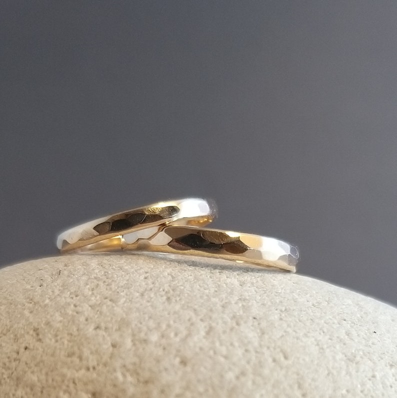 Puede incluir: Dos alianzas de oro martilladas apiladas una encima de la otra sobre una superficie de piedra gris.