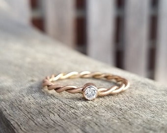Op de afbeelding: Een delicate gouden ring met een gedraaide band en een kleine, heldere diamant in het midden.