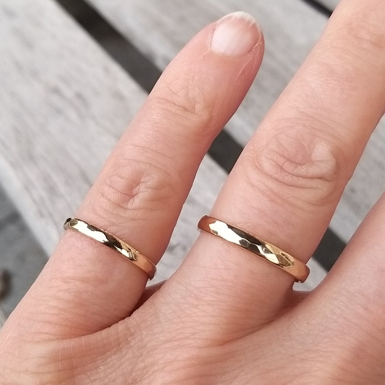 Puede incluir: Dos anillos de oro martillados en un dedo. Los anillos son simples y tienen un acabado texturizado.