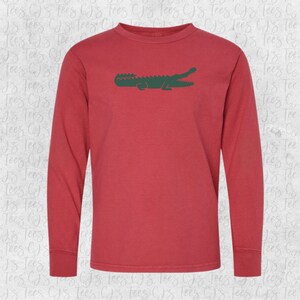 May include: A long-sleeved t-shirt in a red color with a green alligator graphic on the front.