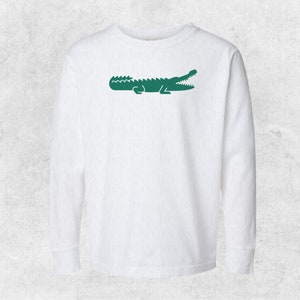 May include: White long-sleeved t-shirt with a green alligator logo on the front.