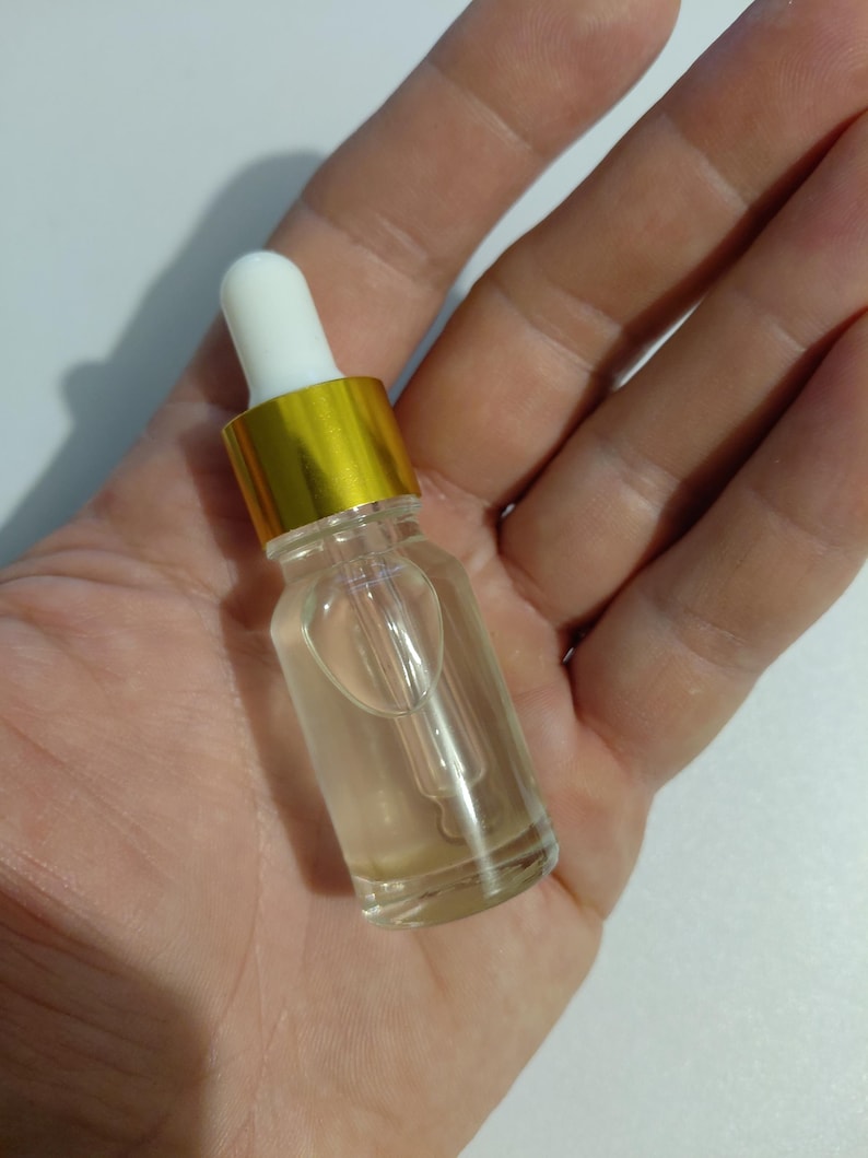 K&ouml;nnte beinhalten: Eine kleine, durchsichtige Glastropfflasche mit einer durchscheinenden Fl&uuml;ssigkeit. Die Flasche hat einen metallisch goldenen Verschluss und einen wei&szlig;en Gummisauger an der Oberseite, der an einer Glaspipette befestigt ist, die in den Beh&auml;lter ragt.