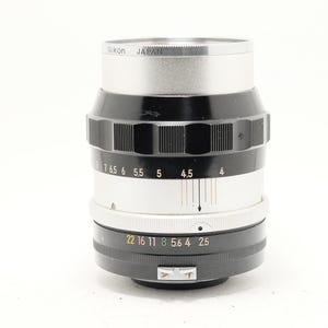 May include: A Nikon camera lens with a silver top, black centre, and white and black rings. The lens has various numerical markings and the text "Nikon JAPAN".
