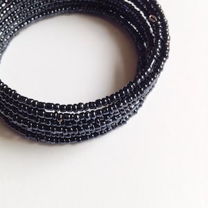 Op de afbeelding: Een zwarte kralen armband met meerdere rijen kralen. De armband is gemaakt van kleine, ronde kralen die stevig aan elkaar zijn geweven.