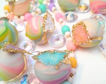 Puede incluir: Una cadena de cuentas de colores con adornos de color pastel con un patrón de espiral. Cada adorno tiene un acento de cristal brillante con borde dorado.