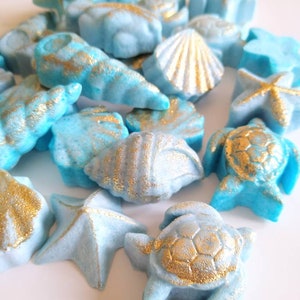 May include: A collection of blue and gold seashell bath bombs. The bath bombs are shaped like seashells, starfish, and sea turtles.