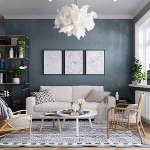 May include: A living room interior with a white sofa, two wicker chairs, a white coffee table, and a black and white patterned rug. The walls are painted a dark blue color and there are three framed black and white line drawings of flowers on the wall. A white fluffy light fixture hangs from the ceiling.