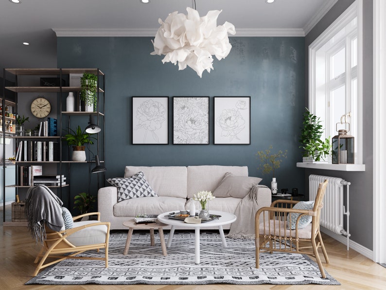 May include: A living room interior with a white sofa, two wicker chairs, a white coffee table, and a black and white patterned rug. The walls are painted a dark blue color and there are three framed black and white line drawings of flowers on the wall. A white fluffy light fixture hangs from the ceiling.