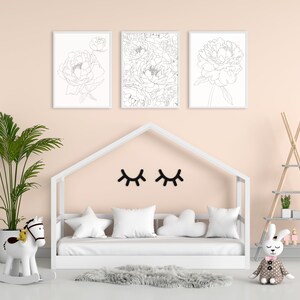May include: A white wooden bed frame with a white mattress and pillows. There are three black and white line drawings of peonies on the wall above the bed. A white rocking horse and a stuffed bunny are on the floor in front of the bed.