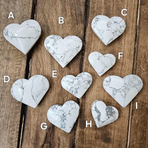 May include: Nine white heart-shaped stones with gray veining. The stones are arranged in a semi-circle on a wooden surface.