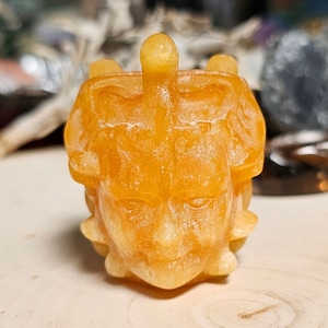 May include: A yellow resin sculpture of a face with a crown-like top. The sculpture has a detailed, textured surface.