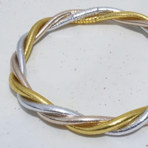 Könnte beinhalten: Ein geflochtenes Armband mit drei Strängen in Gold, Silber und Roségold. Die Stränge sind miteinander verflochten, um ein verdrehtes Design zu erzeugen. Das Armband ist ein Modeaccessoire.