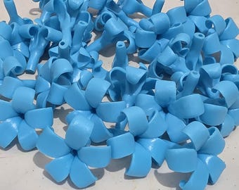 May include: A collection of light blue, flower-shaped embellishments. The plastic flowers are arranged on a white, scalloped-edge plate. Each flower has multiple petals and a central stem, creating a decorative and whimsical appearance.