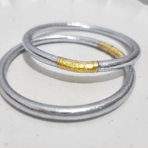 Puede incluir: Dos brazaletes plateados con una banda dorada alrededor del centro de cada brazalete.