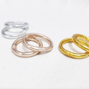 Puede incluir: Tres anillos metálicos simples, uno plateado, uno dorado y uno de oro rosa. Los anillos están apilados uno encima del otro.