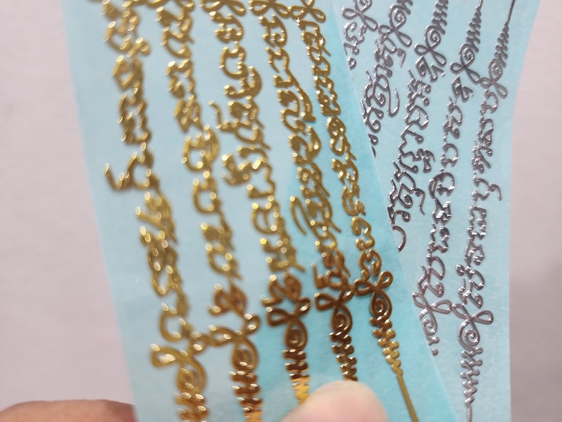 May include: Five gold and silver decorative stickers with intricate designs and lettering on a light blue background.