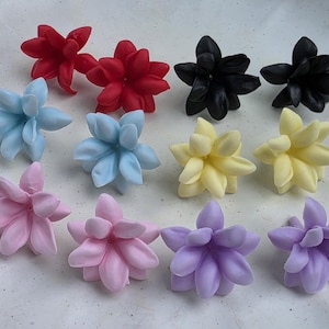 Puede incluir: Una colección de flores suculentas artificiales de colores variados. El surtido incluye flores rojas, negras, azul claro, amarillas, rosas y moradas, dispuestas sobre una superficie blanca. Estas flores decorativas son ideales para manualidades o decoración del hogar.