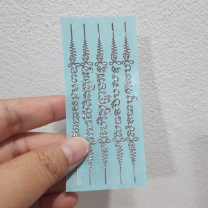 May include: Four silver temporary tattoos on a light blue background. The tattoos feature intricate designs and text in the Thai language.