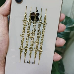 May include: A white iPhone with a gold Apple logo and five gold decorative stickers with intricate designs and text in a foreign language. The text on the stickers reads "នរសពិតប្រា", "នបរិសុទ្ធោមអ", "លធ៩បបស", and "នមពទ្យ".