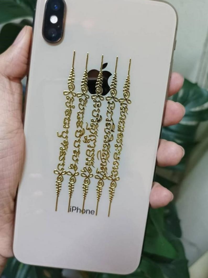 May include: A white iPhone with a gold Apple logo and five gold decorative stickers with intricate designs and text in a foreign language. The text on the stickers reads "នរសពិតប្រា", "នបរិសុទ្ធោមអ", "លធ៩បបស", and "នមពទ្យ".