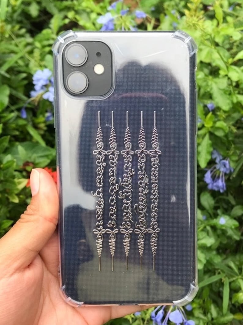 May include: A clear phone case with a black background and silver lettering. The lettering is in a traditional Thai script.