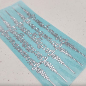May include: A sheet of silver-colored decorative stickers with intricate designs. The stickers are on a light blue background.