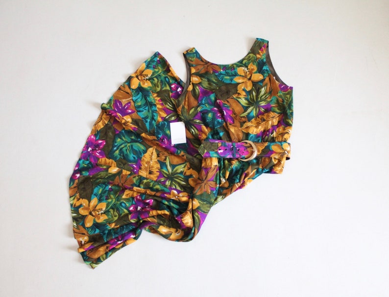 May include: A sleeveless maxi dress with a floral print in shades of yellow, green, purple, and brown. The dress has a belt with a gold buckle.