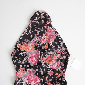 May include: A black halter top with a floral print in shades of pink, orange, and white. The top has a high neckline and a fitted silhouette.