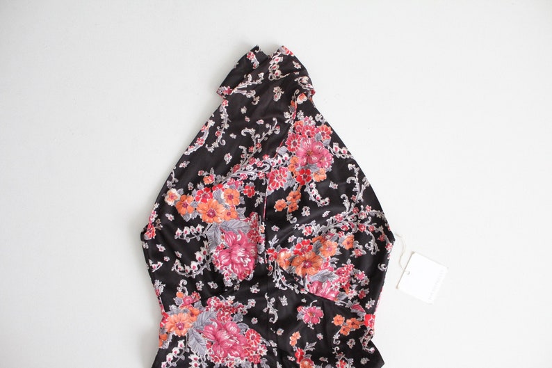 May include: A black halter top with a floral print in shades of pink, orange, and white. The top has a high neckline and a fitted silhouette.