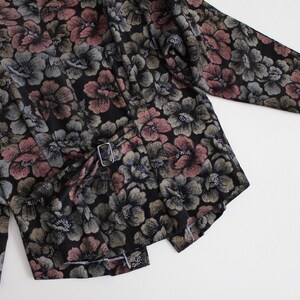 May include: A black long-sleeved jacket with a floral print in shades of pink, green, and silver. The jacket has a belt with a silver buckle.