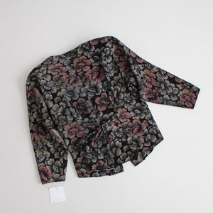 May include: A black floral print blouse with long sleeves and a tie belt. The flowers are in shades of pink, green, and blue.