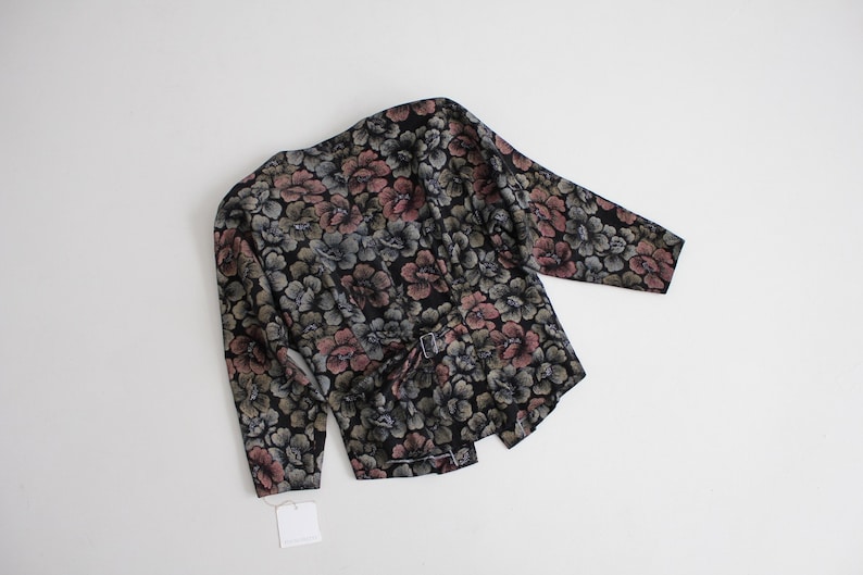 May include: A black floral print blouse with long sleeves and a tie belt. The flowers are in shades of pink, green, and blue.
