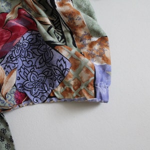 May include: A colorful fabric with a patchwork design featuring floral and geometric patterns in shades of red, blue, green, brown, and white.