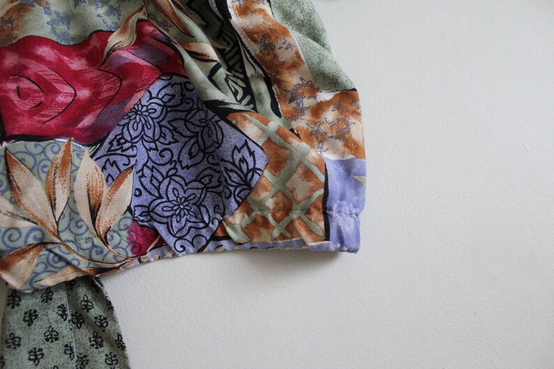 May include: A colorful fabric with a patchwork design featuring floral and geometric patterns in shades of red, blue, green, brown, and white.