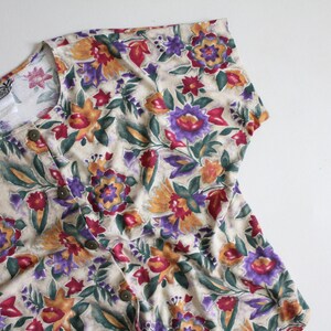 May include: A beige button-up shirt with a floral print featuring shades of purple, red, orange, and green.