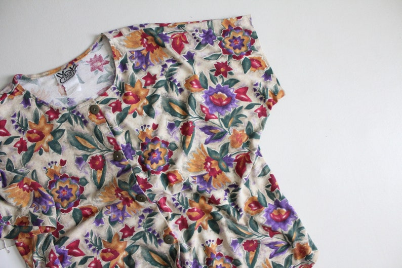 May include: A beige button-up shirt with a floral print featuring shades of purple, red, orange, and green.