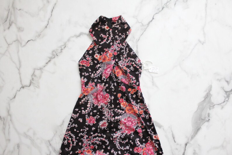 May include: A black halter dress with a floral print in shades of pink, orange, and grey. The dress has a fitted bodice and a flowing skirt.
