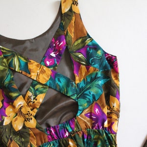 May include: A sleeveless maxi dress with a tropical floral print in shades of yellow, green, purple, and brown. The dress features a criss-cross back design with a cutout detail.
