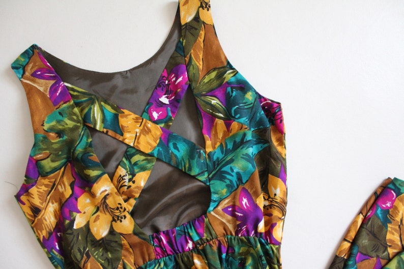 May include: A sleeveless maxi dress with a tropical floral print in shades of yellow, green, purple, and brown. The dress features a criss-cross back design with a cutout detail.