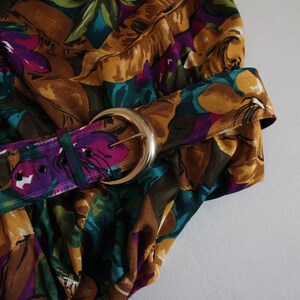 May include: A brown, purple and green floral print fabric with a gold belt buckle.