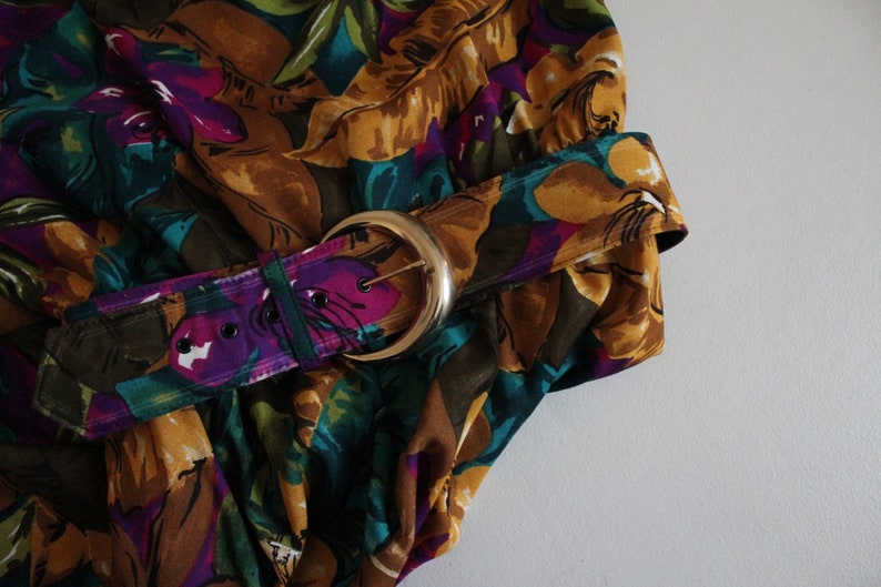 May include: A brown, purple and green floral print fabric with a gold belt buckle.
