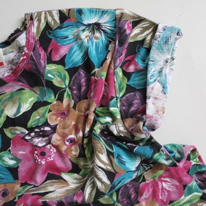 May include: A black short-sleeved shirt with a floral print featuring pink, blue, and green flowers on a black background. The shirt has a white trim around the neckline.