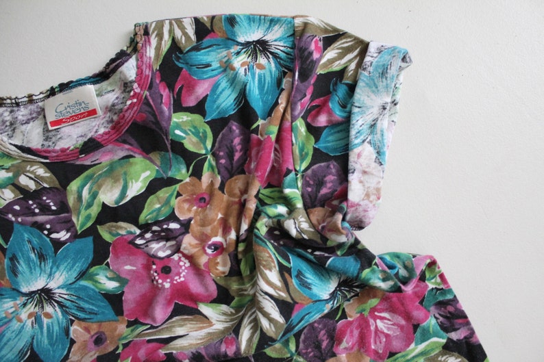 May include: A black short-sleeved shirt with a floral print featuring pink, blue, and green flowers on a black background. The shirt has a white trim around the neckline.