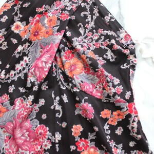 May include: A black dress with a floral print featuring pink, orange, and grey flowers. The dress has a V-neckline and a gathered detail at the bust.